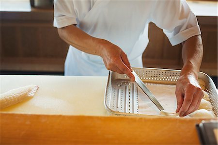 simsearch:6118-09079597,k - High angle close up of chef working at a counter at a Japanese sushi restaurant, placing slices of fish into metal tray. Stock Photo - Premium Royalty-Free, Code: 6118-09079623