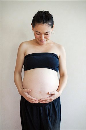 simsearch:6118-08659796,k - A pregnant woman holding her hands under the curve of her stomach, looking down. Stockbilder - Premium RF Lizenzfrei, Bildnummer: 6118-09079788