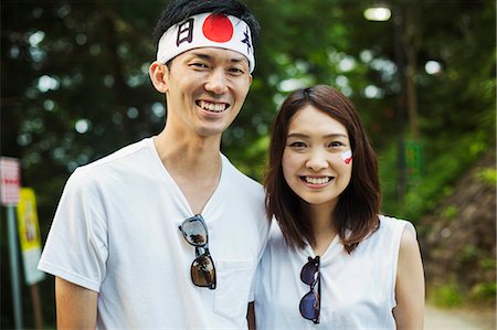 simsearch:6118-09079349,k - Portrait of man wearing headband and young woman with brown hair, Japanese flag painted on her cheek, smiling at camera. Stock Photo - Premium Royalty-Free, Code: 6118-09079791