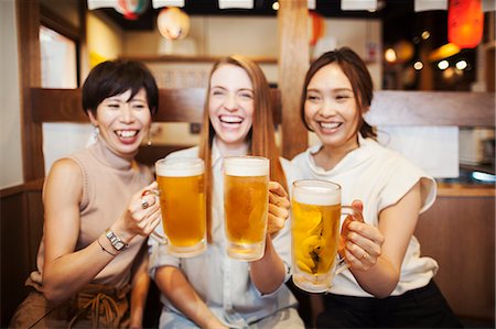 simsearch:6118-09079687,k - Three women sitting sidy by side at a table in a restaurant, holding large glasses with beer. Fotografie stock - Premium Royalty-Free, Codice: 6118-09079709