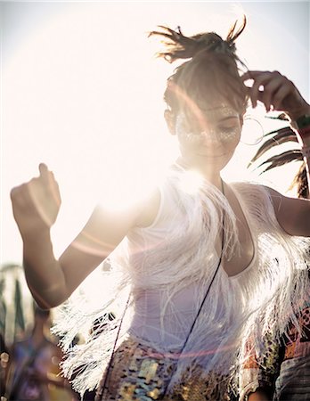 free time - Young woman at a summer music festival in a white vest top with fringes with arms raised, dancing among the crowd. Stock Photo - Premium Royalty-Free, Code: 6118-09018279