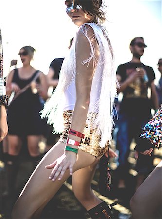 Young woman at a summer music festival wearing golden sequinned hot pants, dancing among the crowd. Stock Photo - Premium Royalty-Free, Code: 6118-09018281