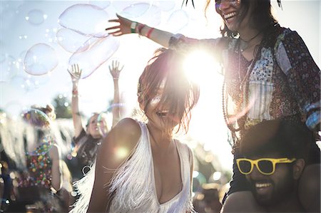 simsearch:6118-09039238,k - Revellers at a summer music festival young man wearing yellow sunglasses carrying woman on his shoulders. Stock Photo - Premium Royalty-Free, Code: 6118-09018293