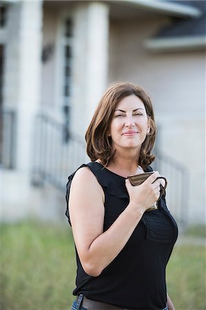 simsearch:6118-09018328,k - A woman in a sleeveless shirt holding a cup in her hands, standing outside a country house. Photographie de stock - Premium Libres de Droits, Code: 6118-09018340