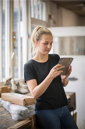 surrey - Woman with blond hair standing in a workshop using a digital tablet, wrapped parcels on a table. Foto de stock - Sin royalties Premium, Código: 6118-09018351