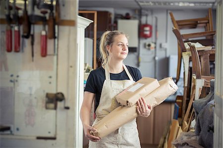 surrey - A young woman in a workshop, holding two packages wrapped in brown packaging paper, ready for despatch. Foto de stock - Sin royalties Premium, Código: 6118-09018355