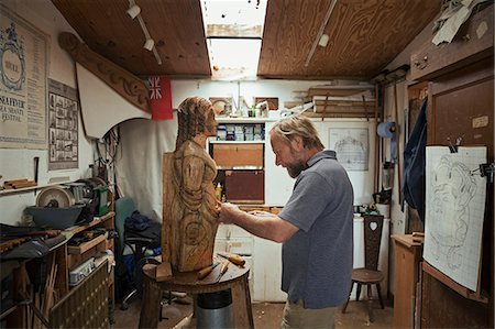 simsearch:6118-09018535,k - A wood carver standing in his workshop, using hand tools to shape and create decoration on a work in progress, a wooden female ship's figurehead. Stock Photo - Premium Royalty-Free, Code: 6118-09018390