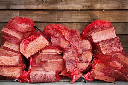 Close up of a stack of firewood in red net bags outside a farm shop. Stock Photo - Premium Royalty-Free, Code: 6118-09018492