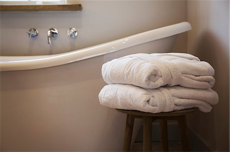 An old fashioned slipper shape bathtub, bath with raised end and wall mounted taps in a bathroom. Two folded guest bathrobes on a stool. Photographie de stock - Premium Libres de Droits, Code: 6118-09018568