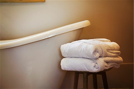 simsearch:6118-09018569,k - An old fashioned slipper shape bathtub, bath with raised end and wall mounted taps in a bathroom. Two folded guest bathrobes on a stool. Foto de stock - Sin royalties Premium, Código: 6118-09018569