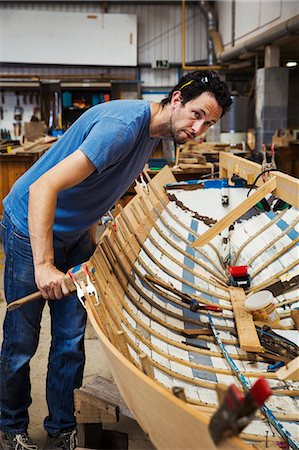 simsearch:6118-08947801,k - Man standing in a boat-builder's workshop, working on a wooden boat hull. Stock Photo - Premium Royalty-Free, Code: 6118-09018516