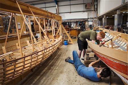 simsearch:6118-09018535,k - Two men in a boat-builder's workshop, working together on a wooden boat hull. Stock Photo - Premium Royalty-Free, Code: 6118-09018521