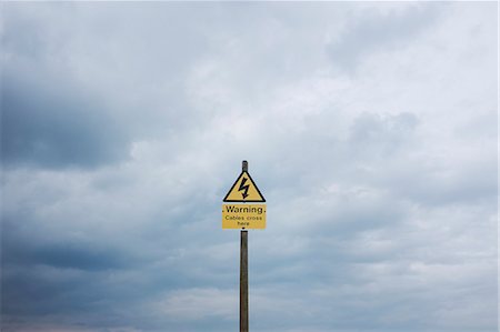 simsearch:6118-08883010,k - Yellow triangular warning sign on pole against cloudy sky. Stockbilder - Premium RF Lizenzfrei, Bildnummer: 6118-09018654