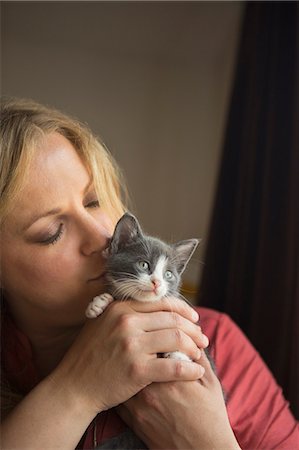 simsearch:6118-09018328,k - Woman holding a small grey and white kitten in her two hands, nuzzling it. Photographie de stock - Premium Libres de Droits, Code: 6118-09018677