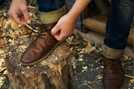 A man in denim jeans with turnups sitting leaning down to tie his shoe laces of his brown leather shoes, one foot up on a splitting block. Foto de stock - Sin royalties Premium, Código: 6118-09018600