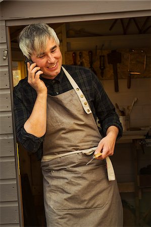 simsearch:6118-09018535,k - Man with grey hair wearing a carpenter's apron standing in doorway of shed, talking on a mobile phone Stock Photo - Premium Royalty-Free, Code: 6118-09018602