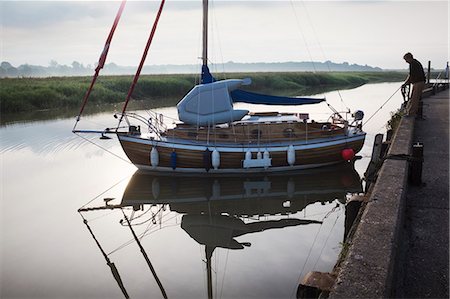 simsearch:6118-08842093,k - Man standing on side of harbour wall, casting off a sailing boat into the river. Stock Photo - Premium Royalty-Free, Code: 6118-09018632