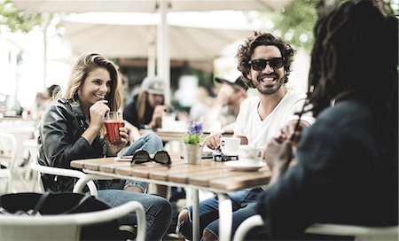 simsearch:6118-08129644,k - Two men and woman sitting outdoors at a table in a cafe, smiling and drinking. Fotografie stock - Premium Royalty-Free, Codice: 6118-09027943