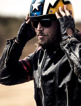 Bearded man wearing black leather jacket and sunglasses adjusting his yellow open face crash helmet. Stock Photo - Premium Royalty-Free, Code: 6118-09027925