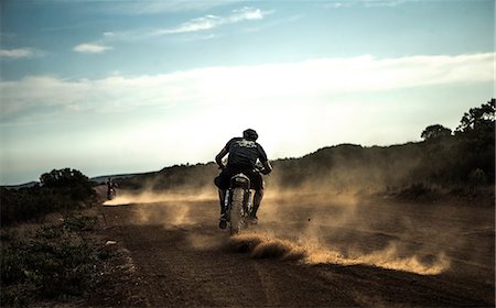 Rear view of man riding cafe racer motorcycle on a dusty dirt road. Stock Photo - Premium Royalty-Free, Code: 6118-09027939
