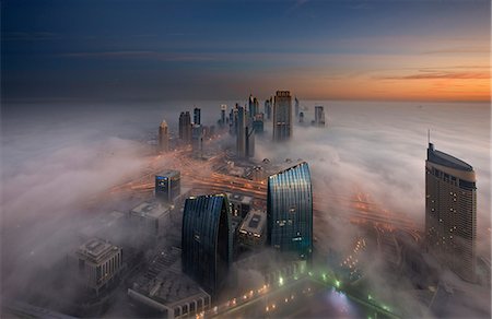 Aerial view of cityscape with illuminated skyscrapers above the clouds in Dubai, United Arab Emirates at dusk. Stock Photo - Premium Royalty-Free, Code: 6118-09028235