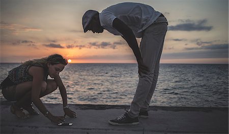 simsearch:6118-08991633,k - Two people looking at a phone placed on the sea wall in front of the ocean. Stock Photo - Premium Royalty-Free, Code: 6118-09039140