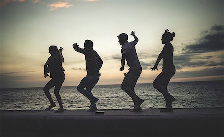 simsearch:6118-08991633,k - Four people dancing in a line on a sea wall in front of the ocean. Stock Photo - Premium Royalty-Free, Code: 6118-09039141