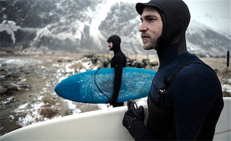 simsearch:6118-09039316,k - Two surfers wearing wetsuits and carrying surfboards standing on a beach with mountains behind. Foto de stock - Sin royalties Premium, Código: 6118-09039183