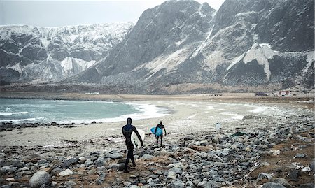 simsearch:6118-09039325,k - Two surfers wearing wetsuits and carrying surfboards walking along a beach with mountains behind. Photographie de stock - Premium Libres de Droits, Code: 6118-09039184