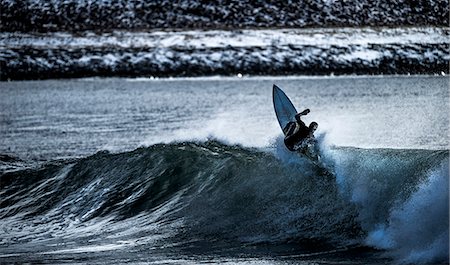 simsearch:6118-09039316,k - A young man surfing on an ocean with a mountain behind. Foto de stock - Sin royalties Premium, Código: 6118-09039194