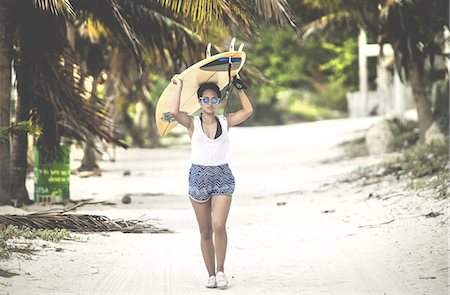 Young woman walking along a beach carrying a surfboard. Stock Photo - Premium Royalty-Free, Code: 6118-09039101