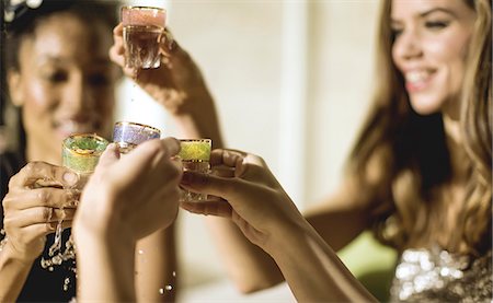 Two young women at a party in sequined dresses drinking and laughing, one wearing a face mask. Fotografie stock - Premium Royalty-Free, Codice: 6118-09039256