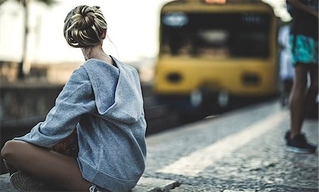 simsearch:6118-09039293,k - Young woman sitting on a railway station platform with a train behind. Photographie de stock - Premium Libres de Droits, Code: 6118-09039286