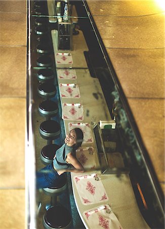 diner bar stool - High angle view of woman sitting at a bar counter looking up at the camera, smiling. Stock Photo - Premium Royalty-Free, Code: 6118-09039341