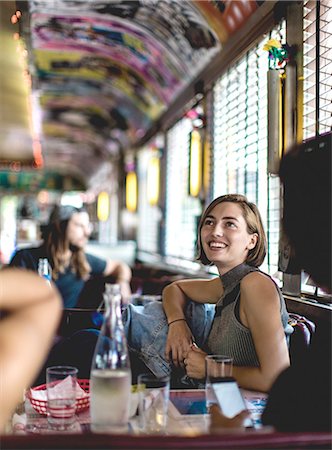 picture of man sitting alone diner - Smiling woman sitting in a booth in a diner looking up and talking to friends. Stock Photo - Premium Royalty-Free, Code: 6118-09039345