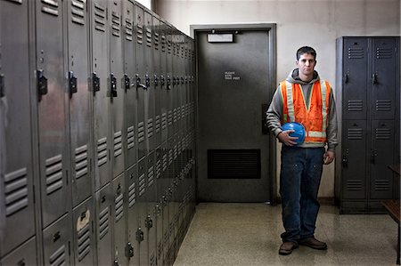 View of a young Caucasian factory worker wearing a safety vest and standing next to lockers in a factory break room. Stock Photo - Premium Royalty-Free, Code: 6118-09140044