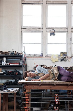sleeping - Black woman factory worker taking a nap on top of a work station in a woodworking factory. Stock Photo - Premium Royalty-Free, Code: 6118-09140127