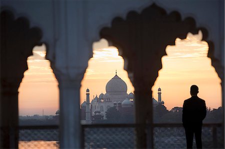 Rear view of man standing underneath scalloped arch on balcony at sunset, Taj Mahal palace and mausoleum in the distance. Stock Photo - Premium Royalty-Free, Code: 6118-09144789