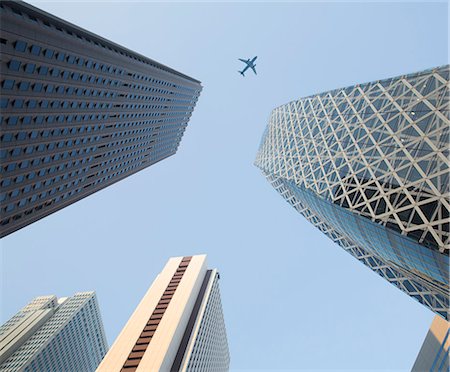 simsearch:6118-09144821,k - Low angle view from urban street towards clear sky, along glass and steel facades of tall skyscrapers, passenger plane going past. Photographie de stock - Premium Libres de Droits, Code: 6118-09144797