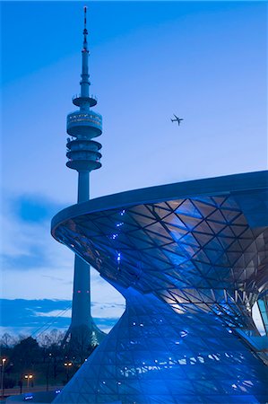 simsearch:400-07445490,k - View of Communications Tower and curved glass facade of contemporary building at night, passenger plane flying past. Stock Photo - Premium Royalty-Free, Code: 6118-09144801