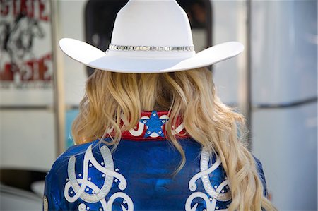 Rear view of woman with long blond hair wearing white Stetson hat and shiny blue jacket decorated with studs and white and red embroidery. Foto de stock - Sin royalties Premium, Código: 6118-09144813