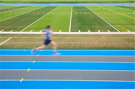 Side view of man running on blue track on sports field, motion blur. Stock Photo - Premium Royalty-Free, Code: 6118-09144834