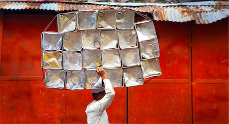 pagliaio - Side view of man carrying stack of metal containers on his head, walking past red metal wall. Fotografie stock - Premium Royalty-Free, Codice: 6118-09144945