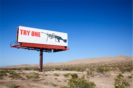 Large board advertising machine gun in the desert. Photographie de stock - Premium Libres de Droits, Code: 6118-09144956