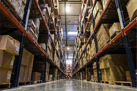 simsearch:6118-09174228,k - View down an aisle of racks holding cardboard boxes of product on pallets  in a large distribution warehouse Fotografie stock - Premium Royalty-Free, Codice: 6118-09147851