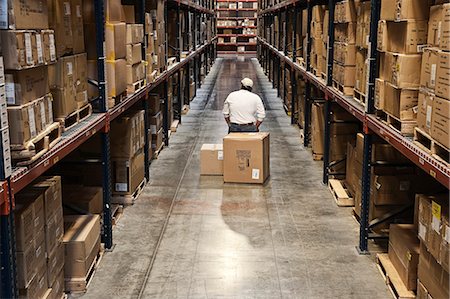 simsearch:6118-09174220,k - Single warehouse worker in between large racks of cardboard boxes on pallets in a large distribution warehouse; Fotografie stock - Premium Royalty-Free, Codice: 6118-09147856