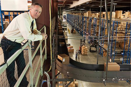 simsearch:6118-09174185,k - Overhead view portrait of a male Caucasian executive in a shirt and tie surrounded by large racks, conveyor belts, forklifts and products stored in cardboard boxes  in a large distribution warehouse. Stockbilder - Premium RF Lizenzfrei, Bildnummer: 6118-09147867