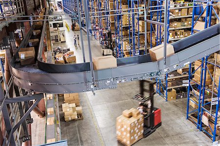 simsearch:6118-09174220,k - Overhead view looking down an aisle of large racks,  conveyor belts and fork lifts,  in a distribution warehouse of cardboard boxes holding products. Fotografie stock - Premium Royalty-Free, Codice: 6118-09147866