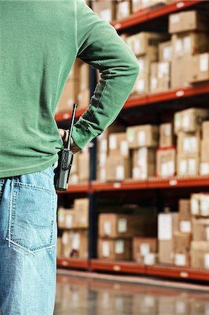 simsearch:628-01878003,k - Closeup of a warehouse worker and a walkie talkie with a large rack of products in cardboard boxes in the background of a large distribution warehouse. Photographie de stock - Premium Libres de Droits, Code: 6118-09147886