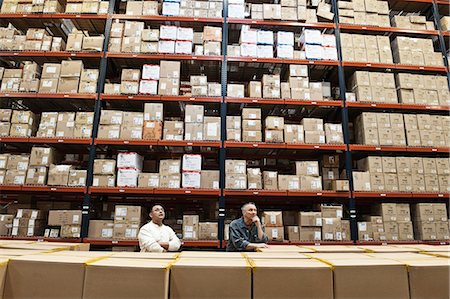 simsearch:600-01519631,k - Two male warehouse workers checking inventory in a large distribution warehouse full of products stored in cardboard boxes on pallets on large racks. Photographie de stock - Premium Libres de Droits, Code: 6118-09147889